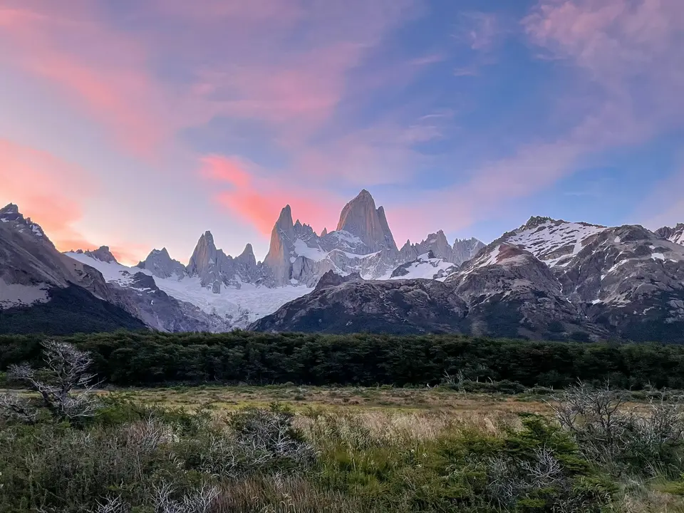 a field with grass and bushes in front of a mountain range — El Chaltén