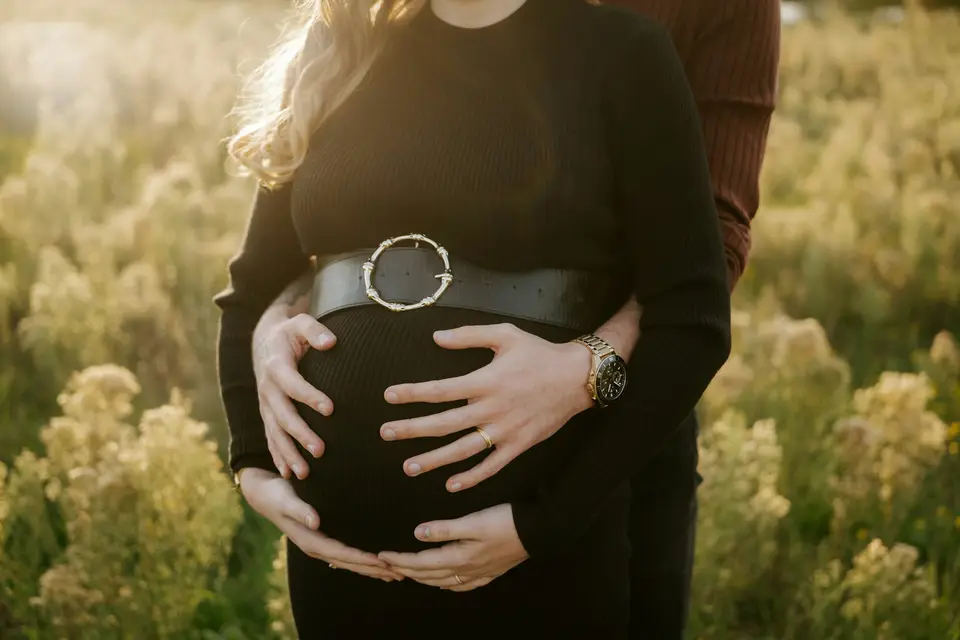 Pregnant woman in black dress with hands on belly